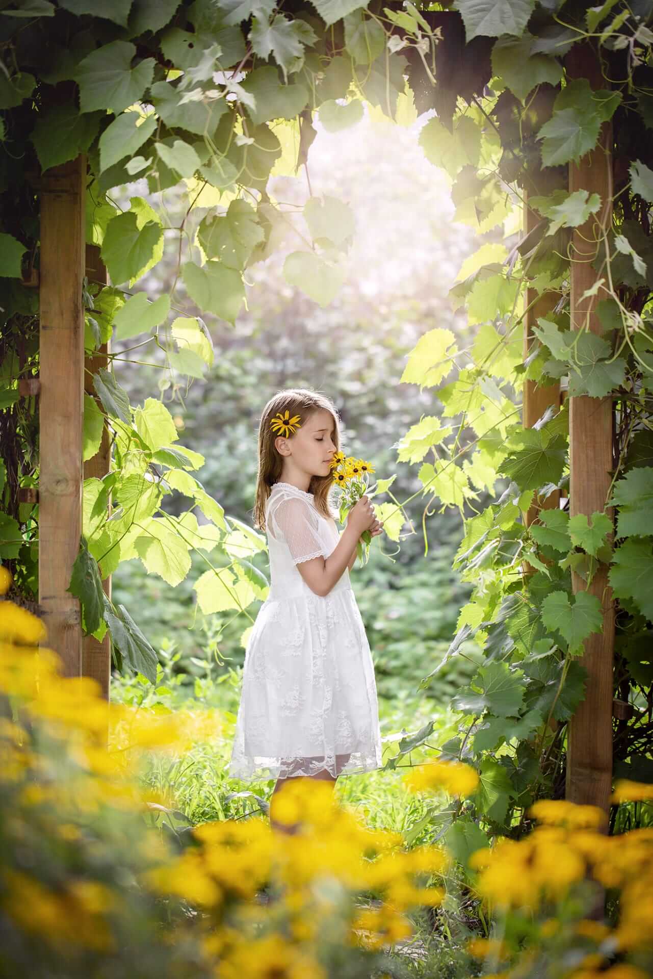 Une petite fille en robe blanche sentant une fleur, capturée par une photographe à Granby.
