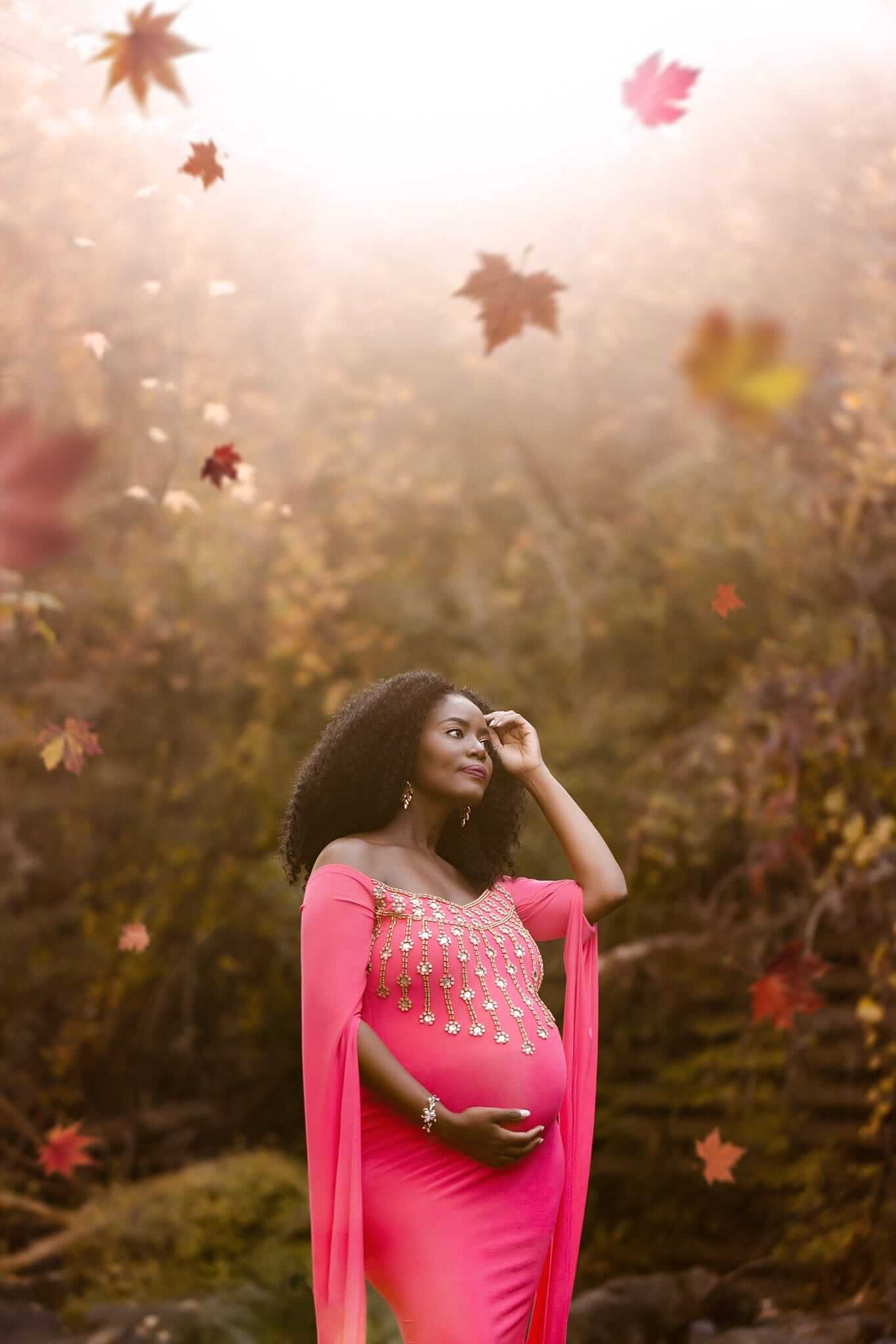Une femme enceinte vêtue d'une robe rose posant devant des feuilles, magnifiquement capturée par une photographe de maternité professionnel basée à Granby.