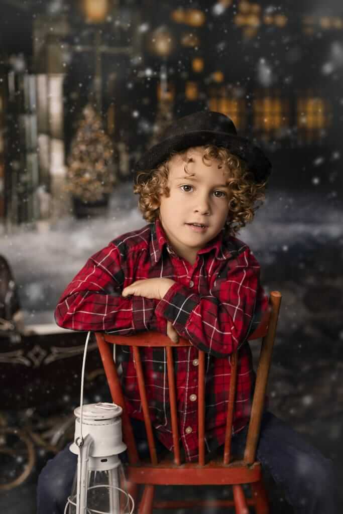 Un jeune garçon assis sur une chaise rouge devant un sapin de Noël.