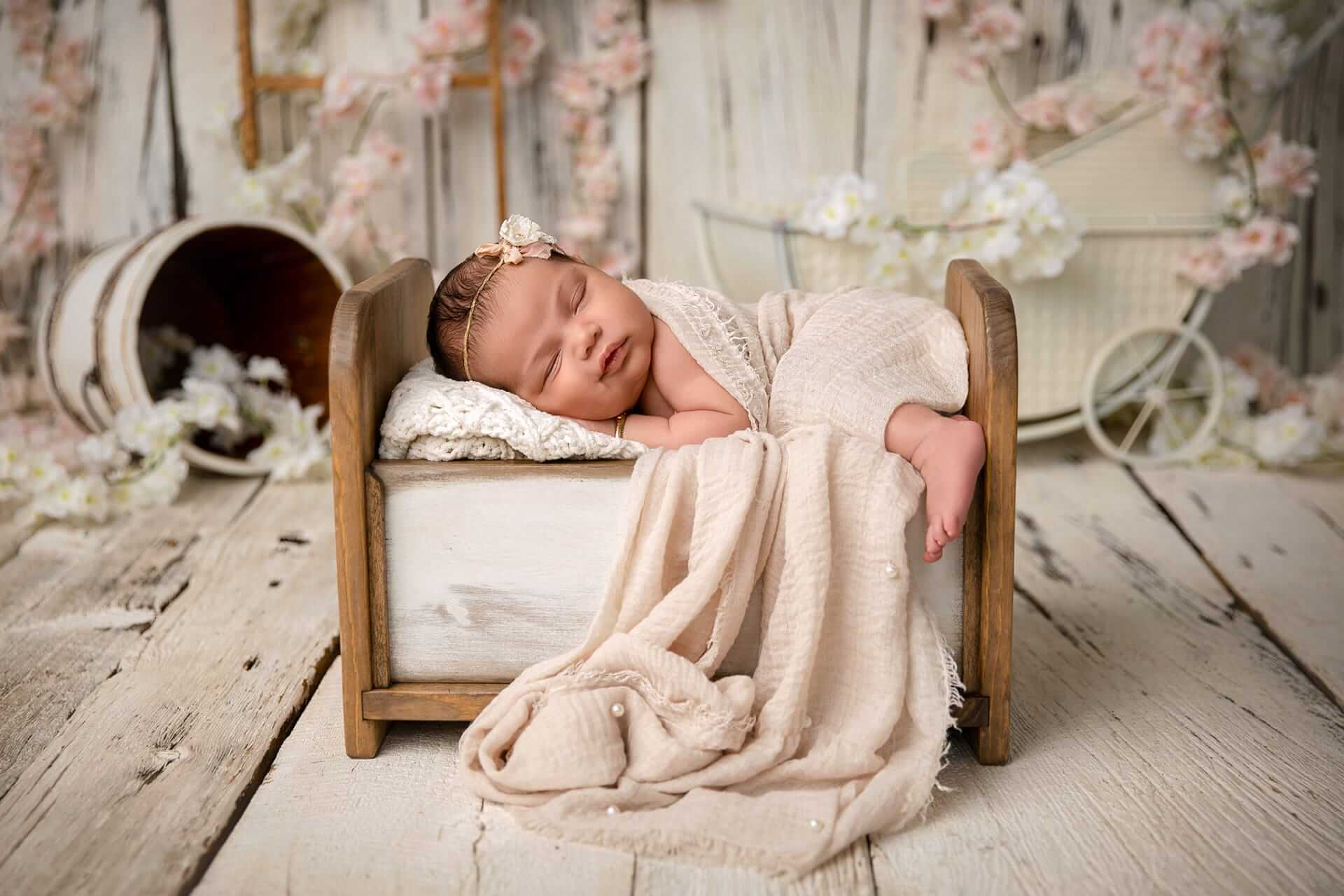 Un photographe capture de magnifiques photos d'un nouveau-né endormi posé dans une boîte en bois, entourée de fleurs.