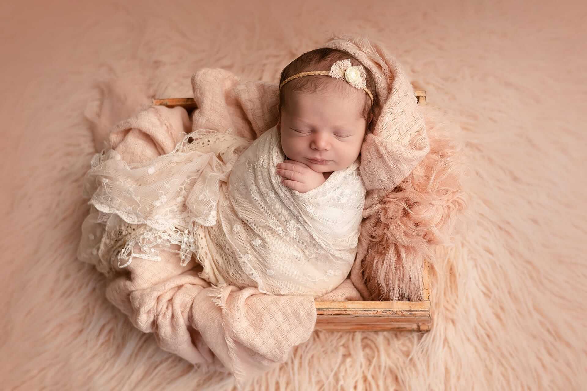 Un bébé fille est enveloppée dans une couverture rose dans une boîte en bois. Le photographe capture de magnifiques photos du nouveau-né.