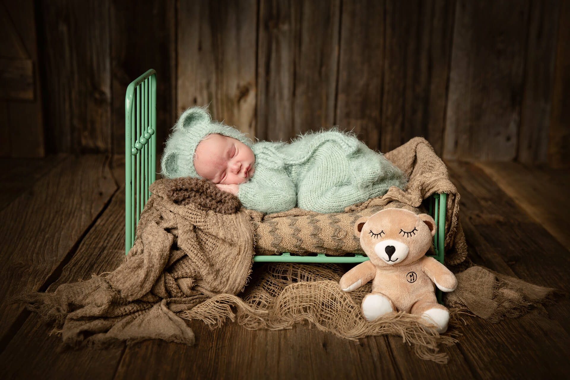 Un bébé dort dans un lit en métal avec un ours en peluche.