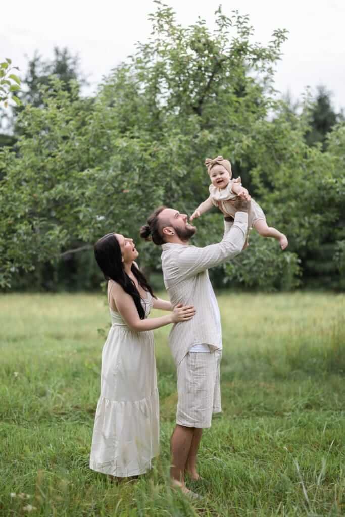 Des parents soulèvent leur bébé dans un verger en fleurs.
