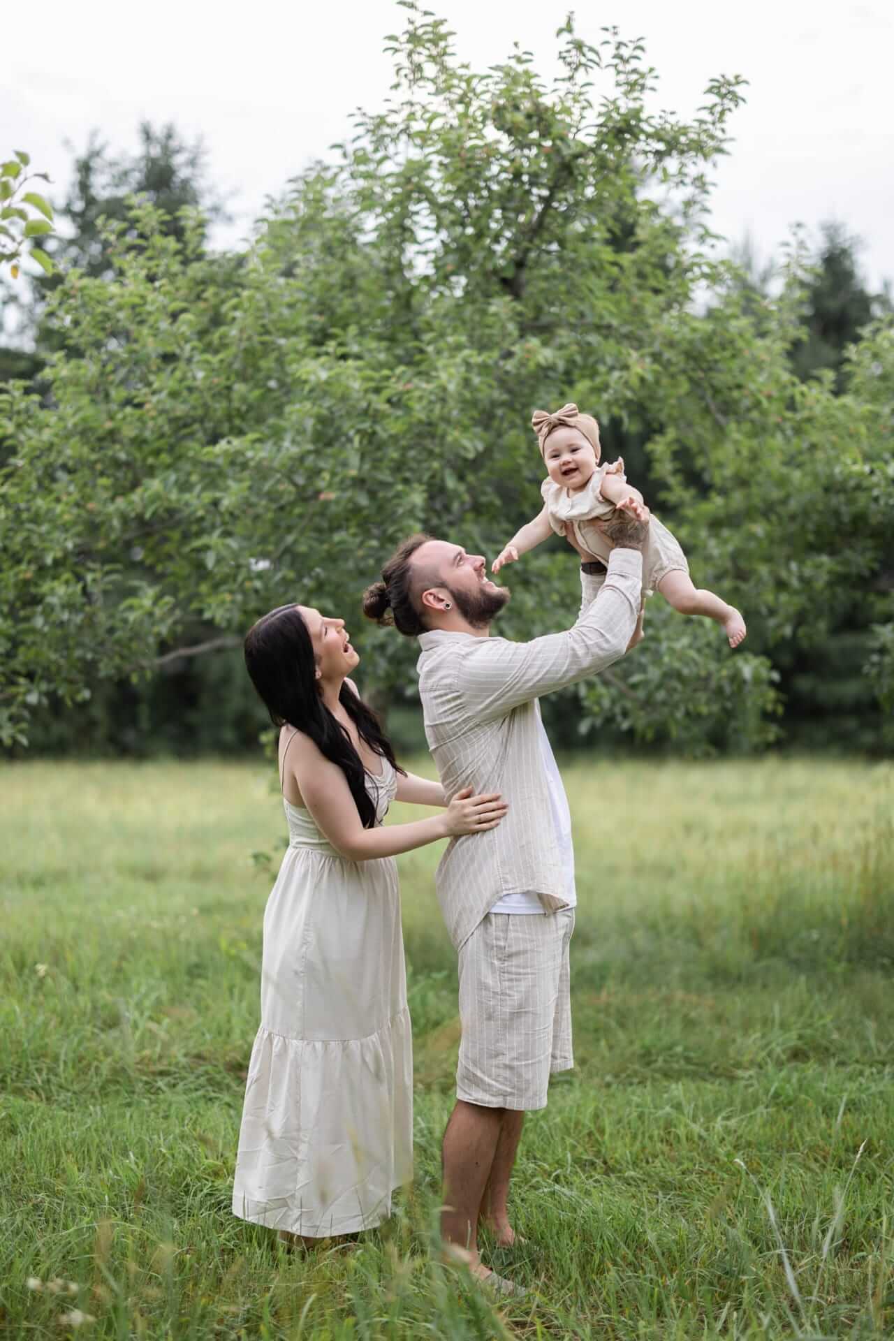 Photo d'une famille tenant leur bébé en l'air dans un verger de pommiers, réalisée par une photographe de Granby.