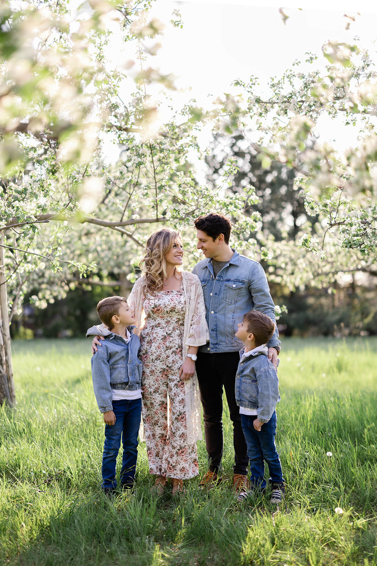 Une famille se tient dans un verger de pommiers avec ses enfants.