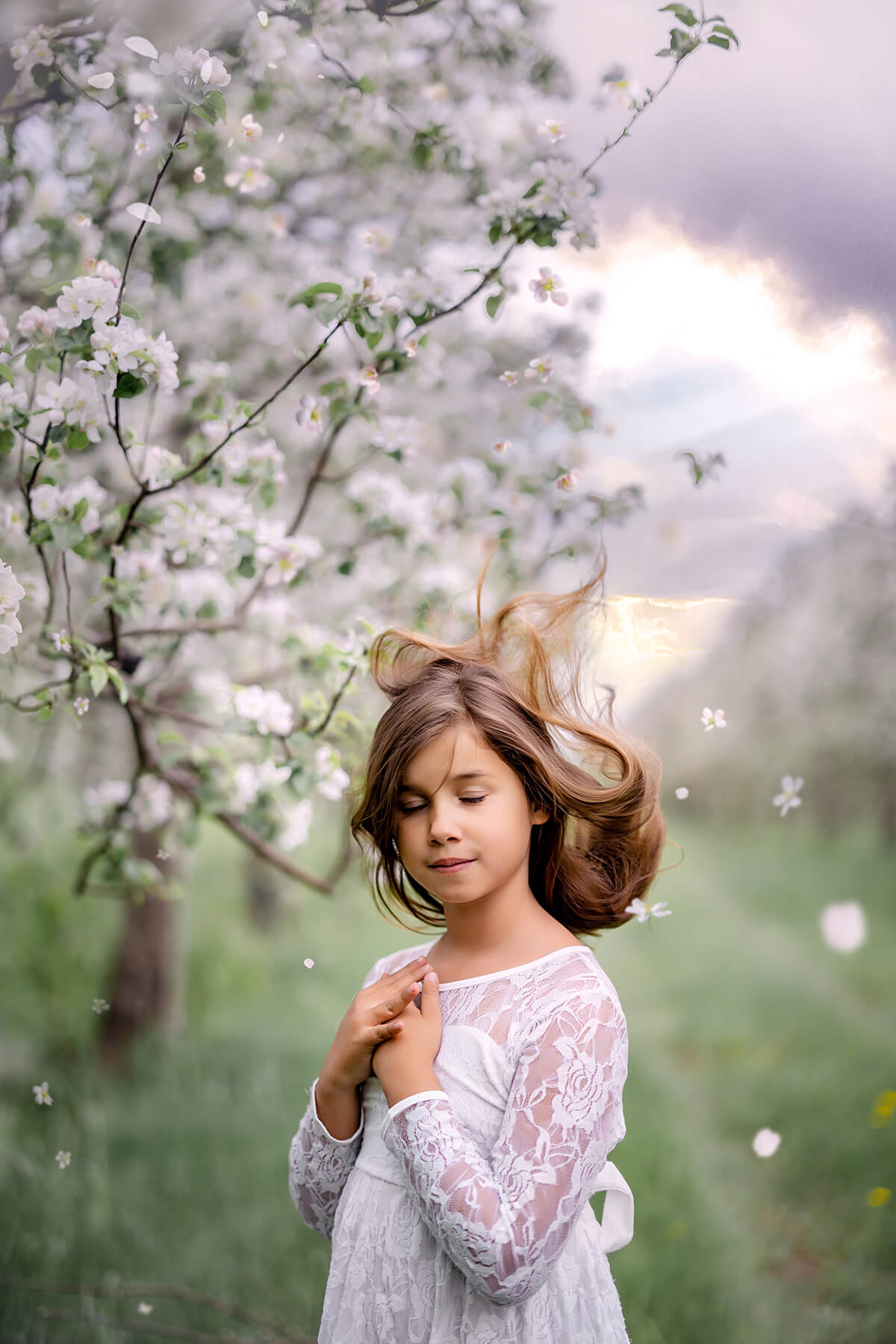 Une petite fille en robe blanche debout dans un verger de pommiers capturée par une photographe spécialisée dans la photographie d'enfants fineart à Granby.