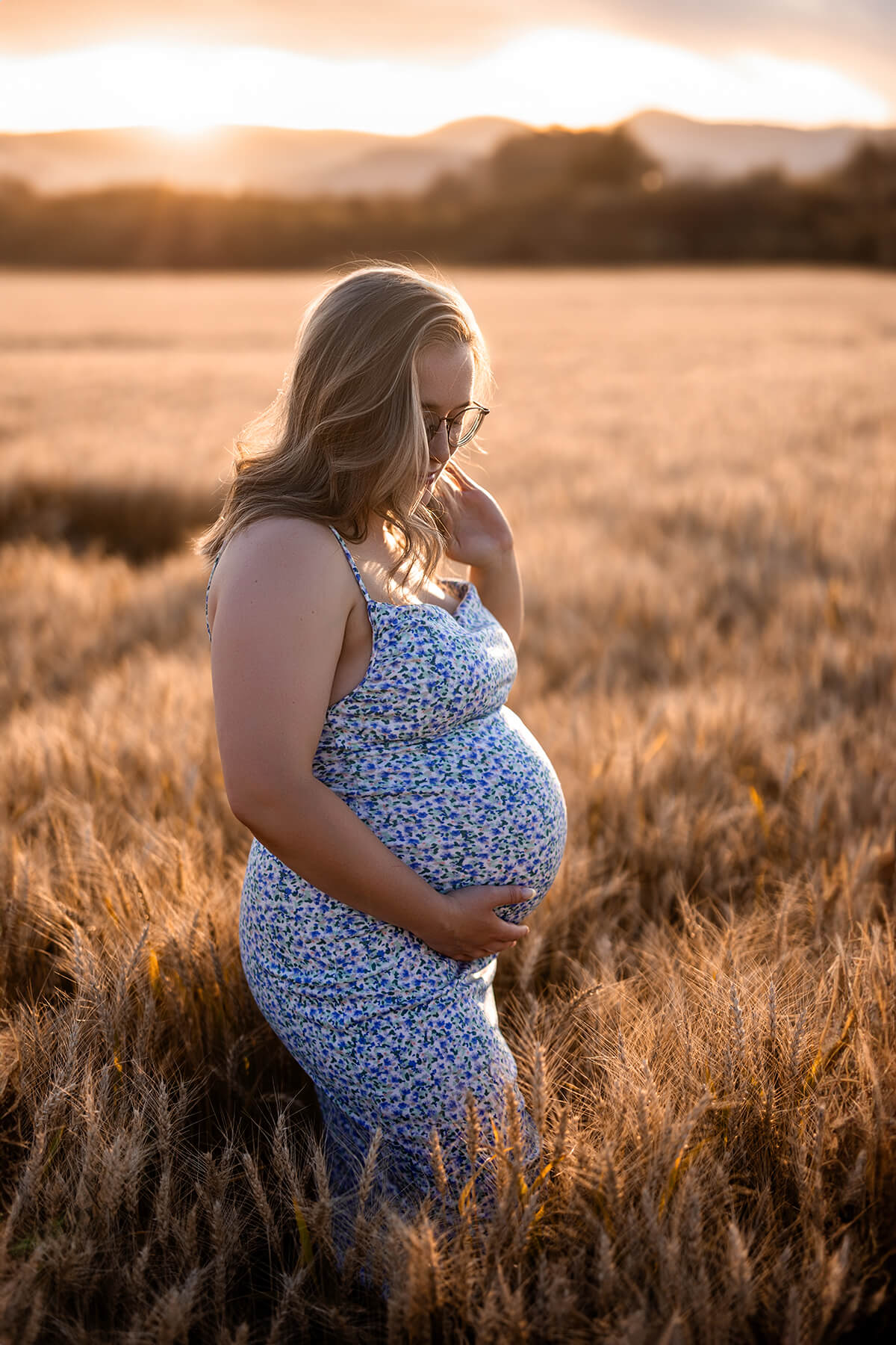 Une femme enceinte debout dans un champ de blé au coucher du soleil.