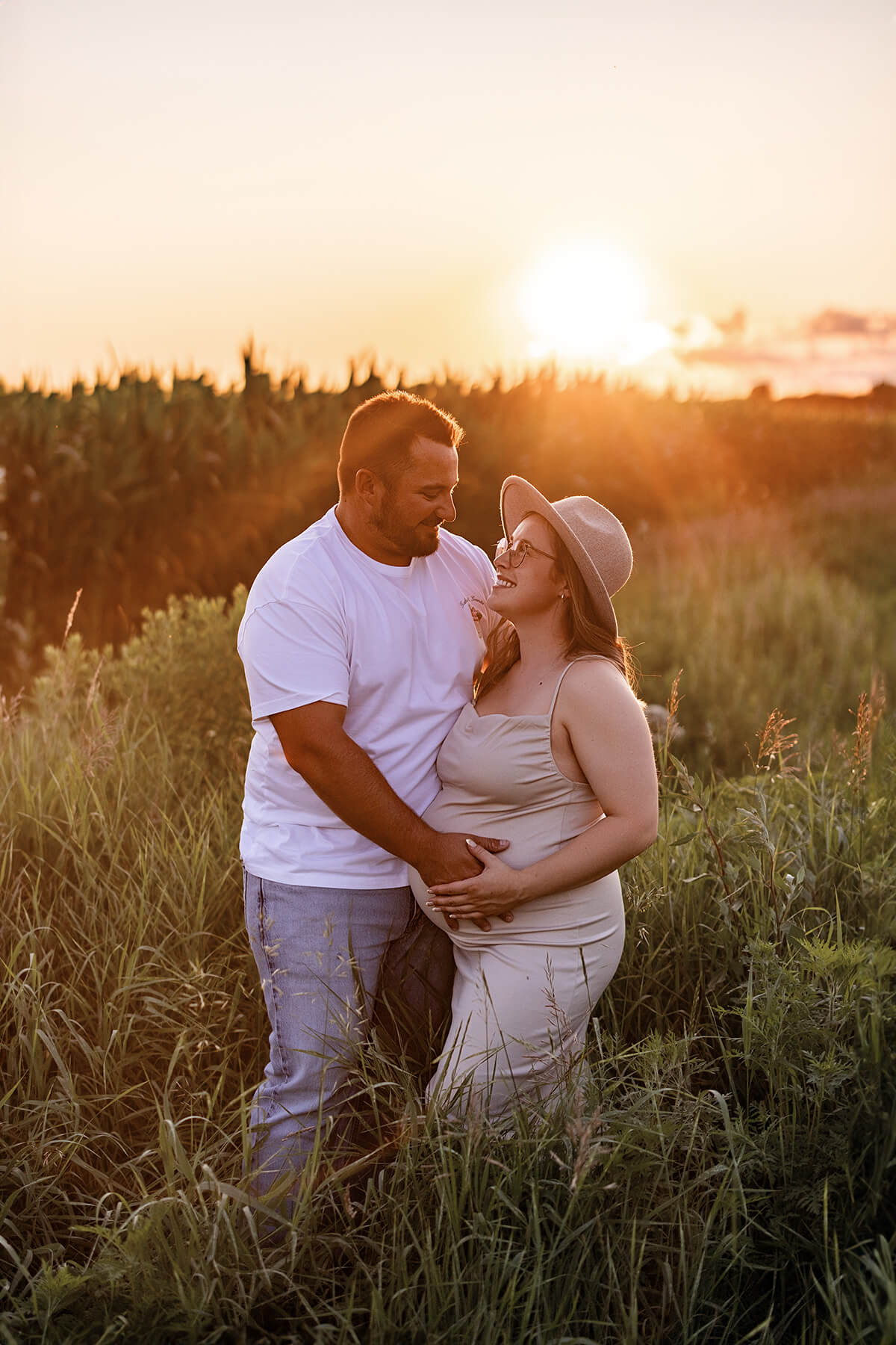 Un couple enceinte debout dans un champ au coucher du soleil, capturé par une talentueuse photographe de maternité à Granby.