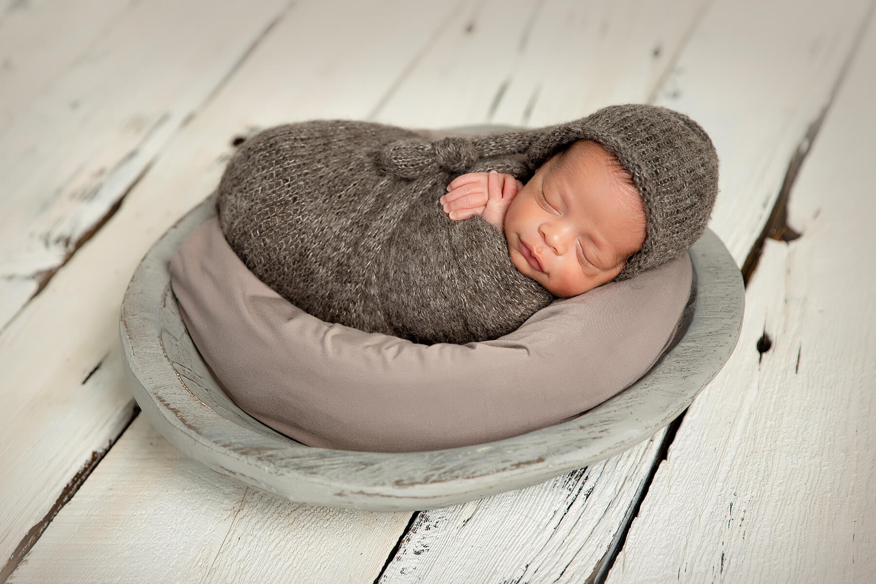 Un photographe capture des photos magnifiques d'un nouveau-né paisiblement endormi dans un bol posé sur un plancher en bois.