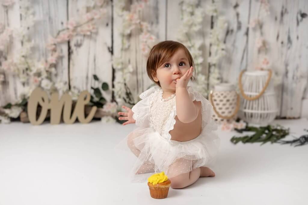 Une petite fille assise par terre avec un cupcake devant elle.