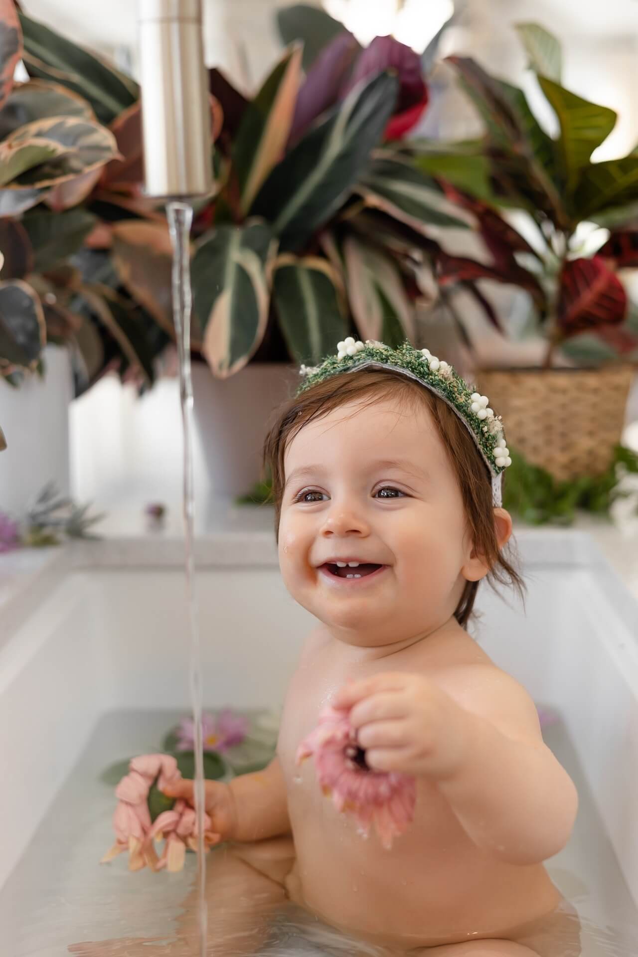 Un bébé dans une baignoire entouré de plantes, capturé par un photographe talentueux à des tarifs abordables.