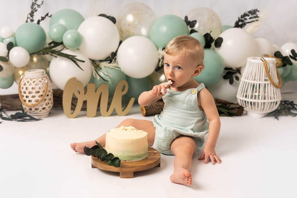 Un bébé mange un gâteau devant des ballons.