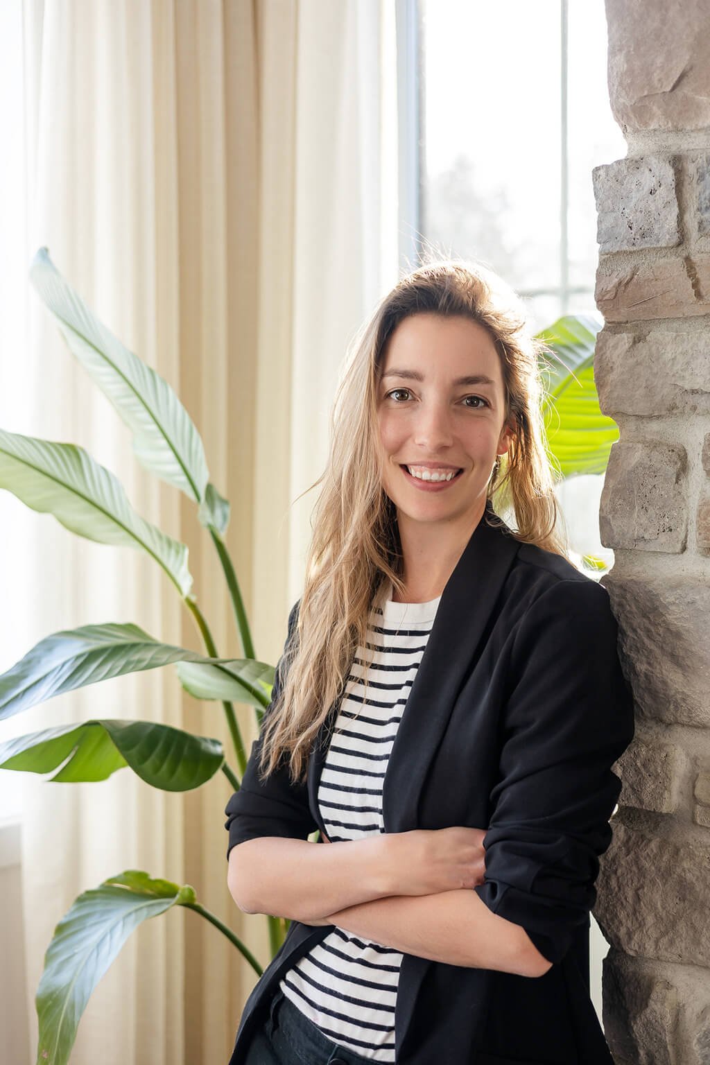 Une femme vêtue d'un blazer noir et d'une chemise rayée debout devant une plante.