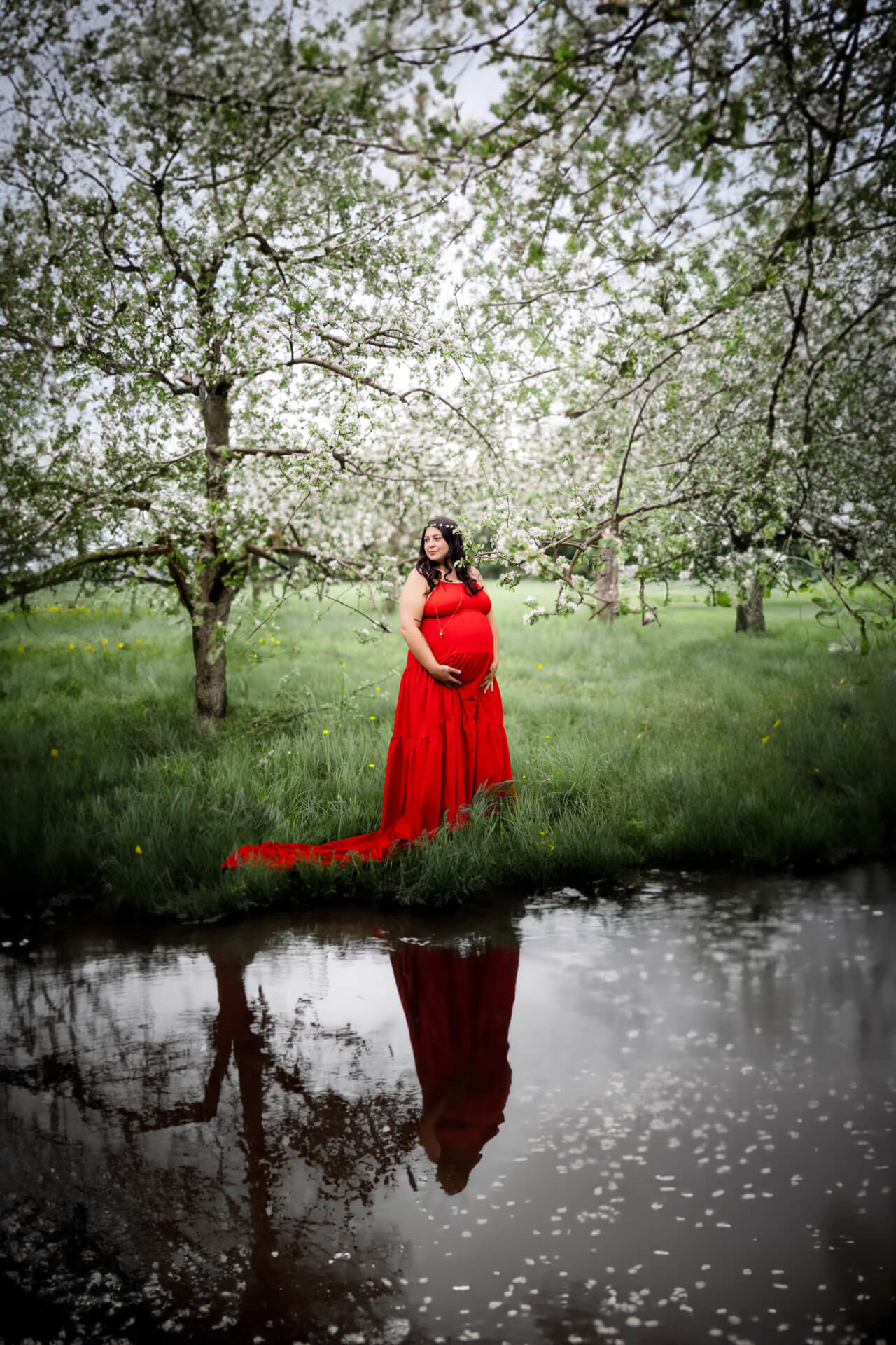 Une femme enceinte vêtue d’une robe rouge debout dans un étang.
