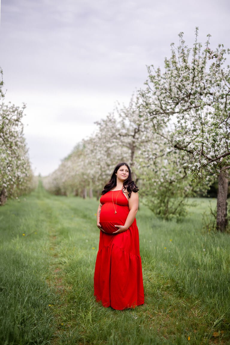 Une femme enceinte vêtue d’une robe rouge debout dans un verger