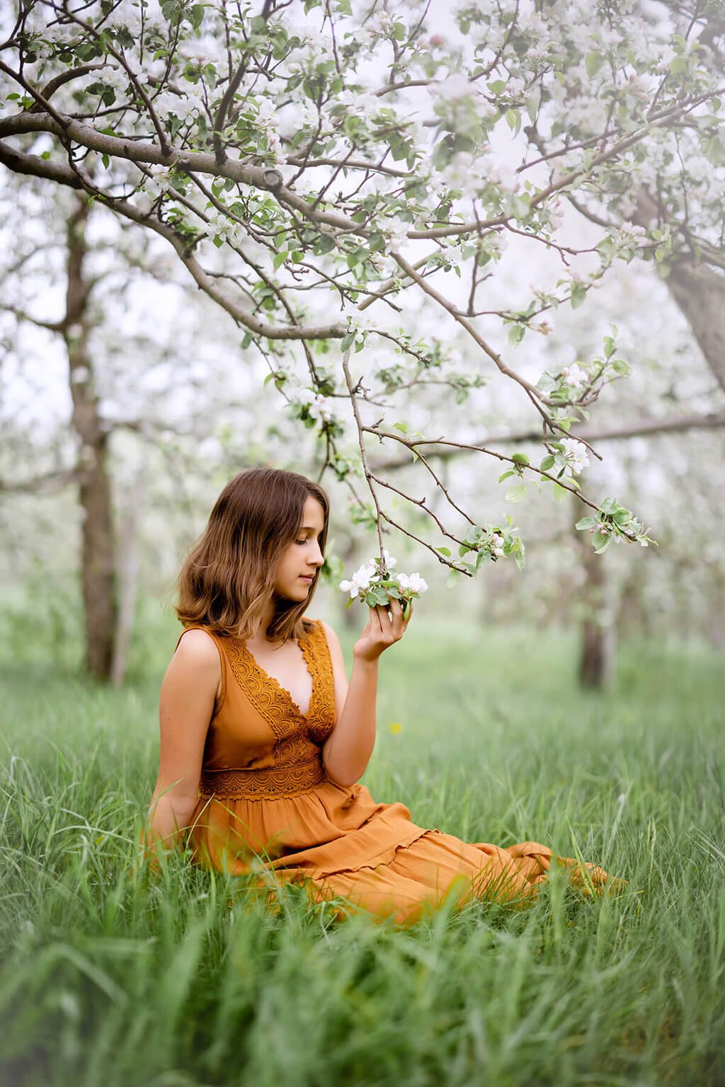 Une femme vêtue d’une robe orange assise dans un verger de pommiers — Rébecca Vandal, photographe à Granby