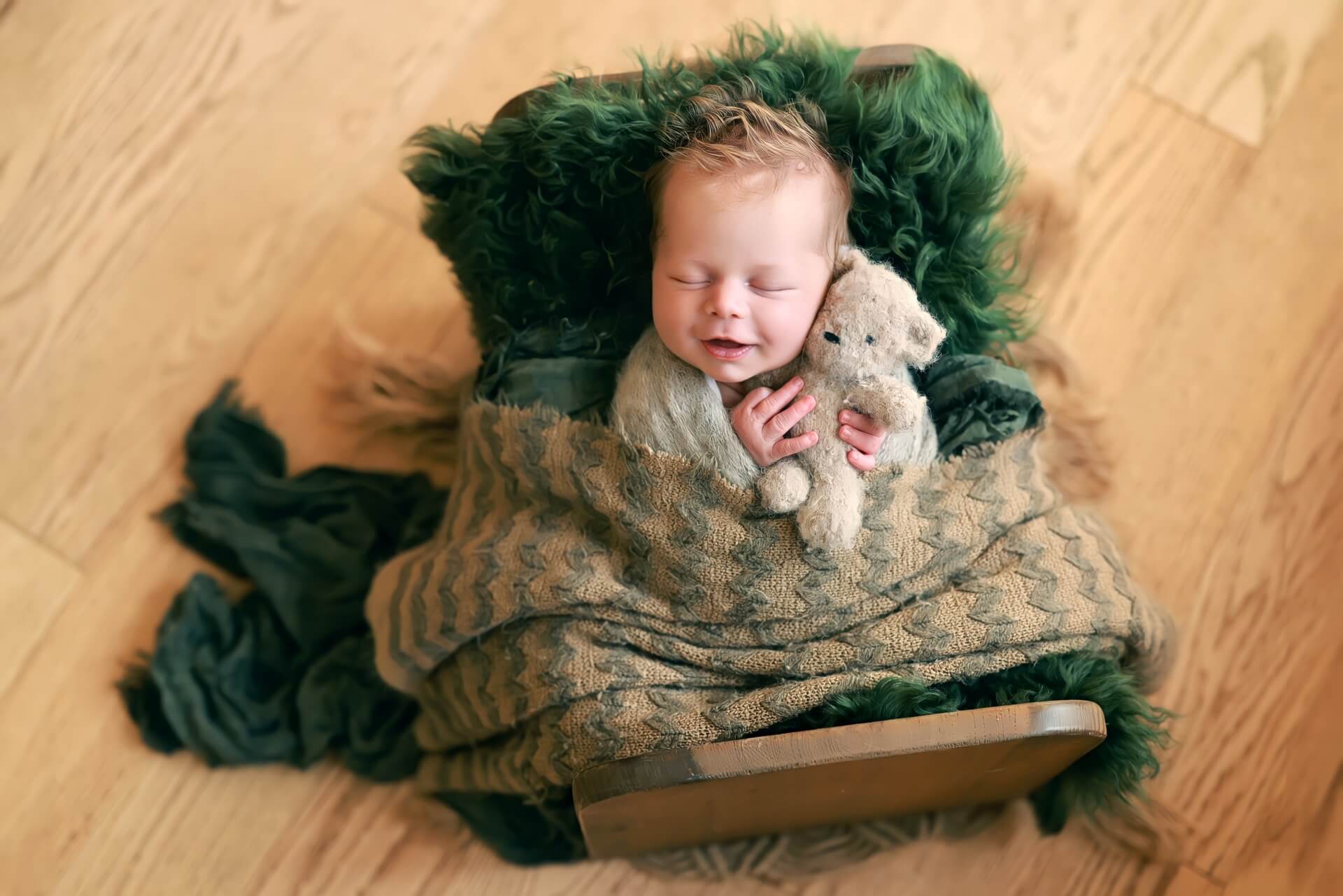 Un bébé dort dans un panier en bois avec un ours en peluche.