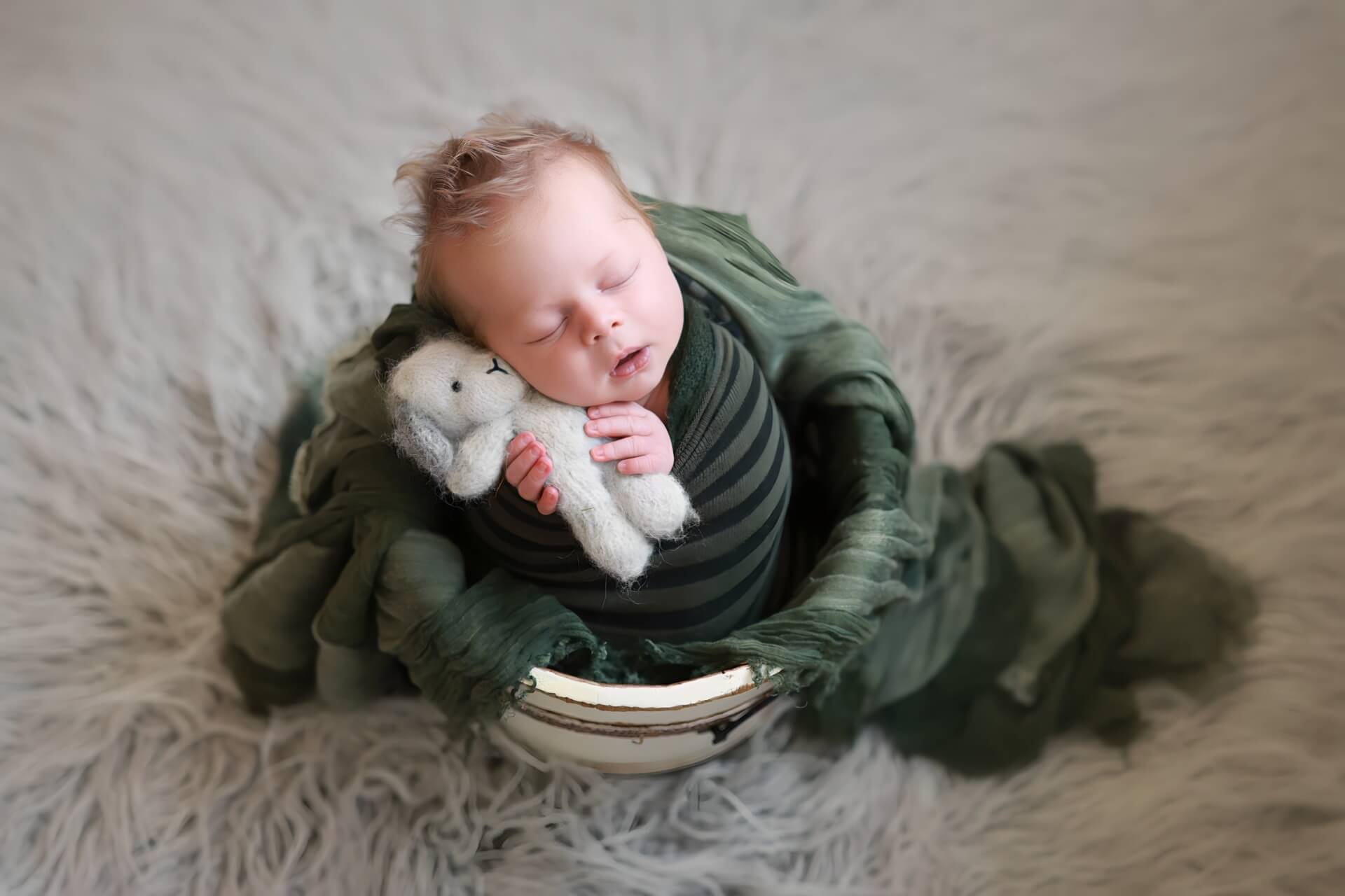 Un bébé dort dans un panier avec un ours en peluche.
