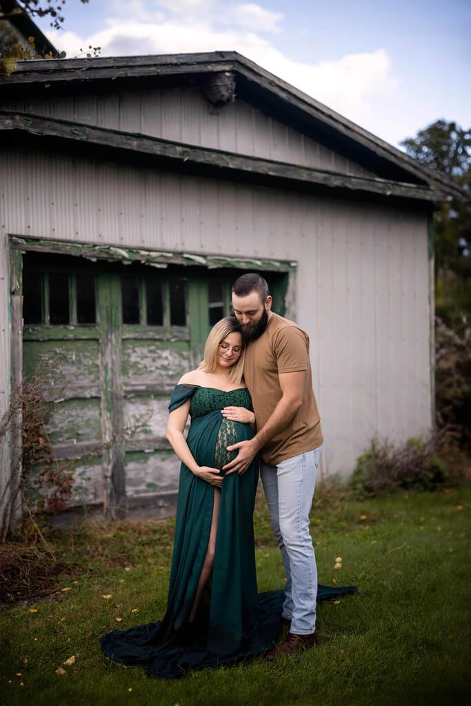 Un couple enceinte debout devant une vieille grange.