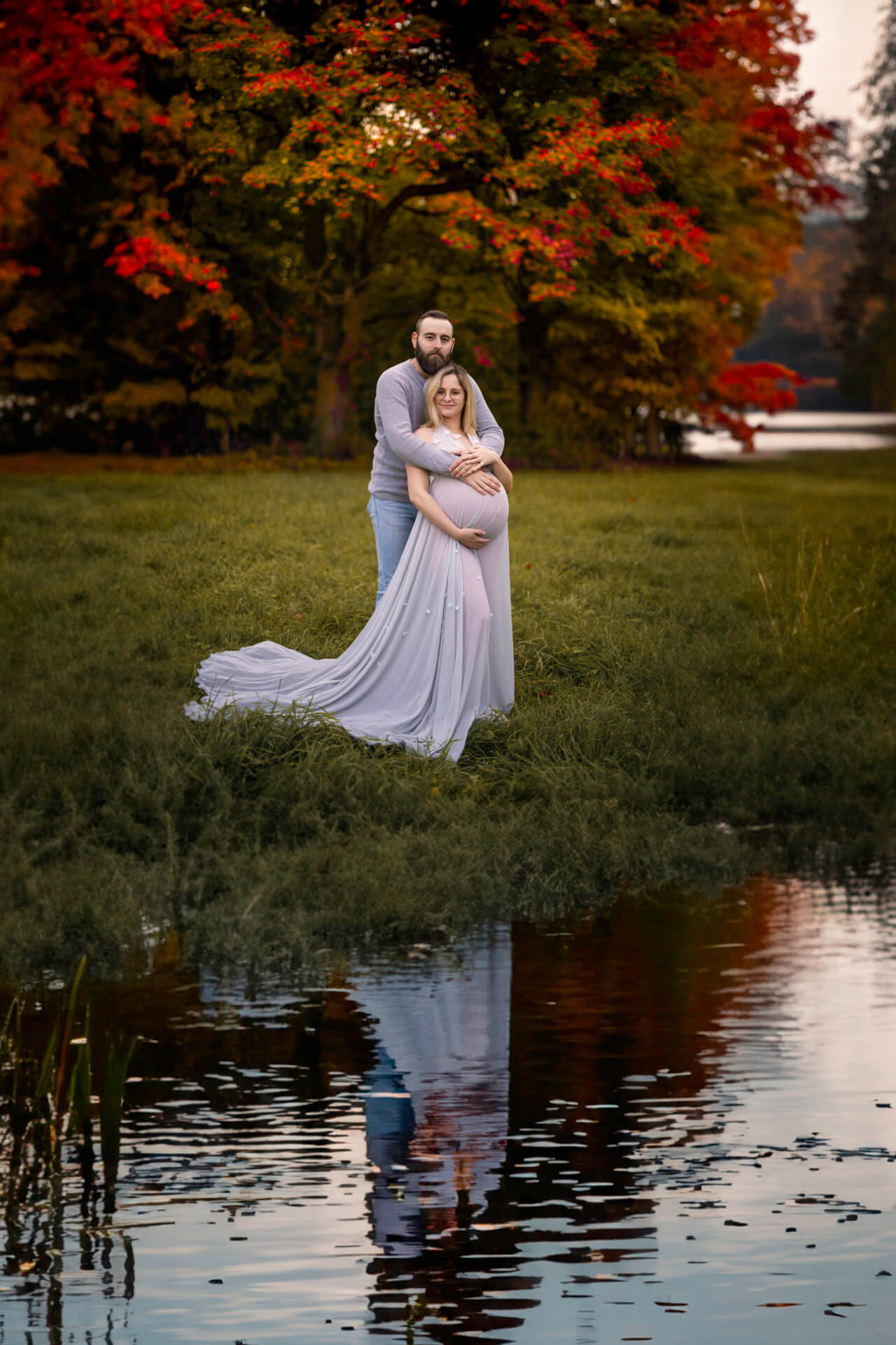 Un couple pose devant un étang avec des arbres en arrière-plan.