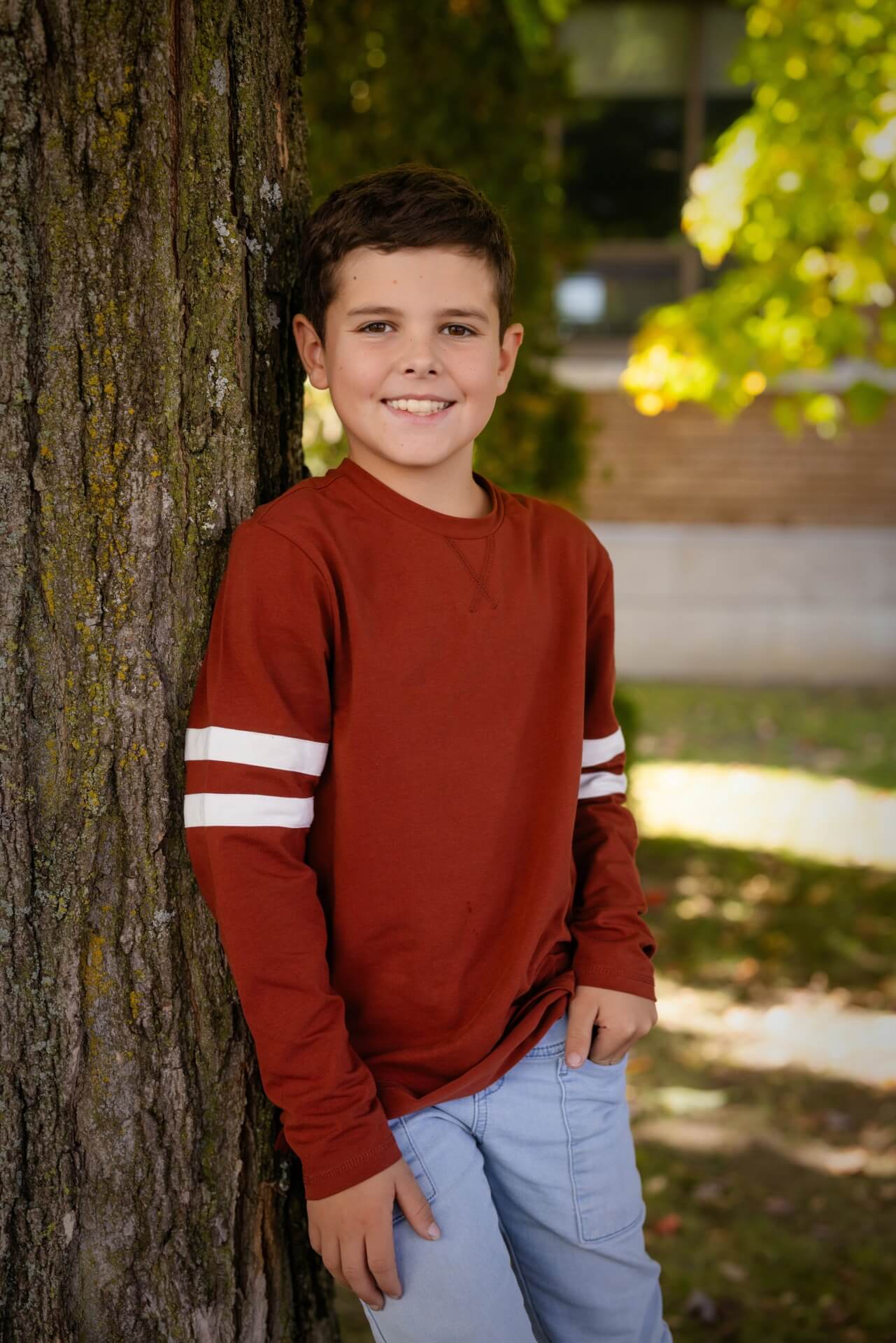 Un jeune garçon posant contre un arbre pour un photographe, capturant l'instant à des tarifs abordables.