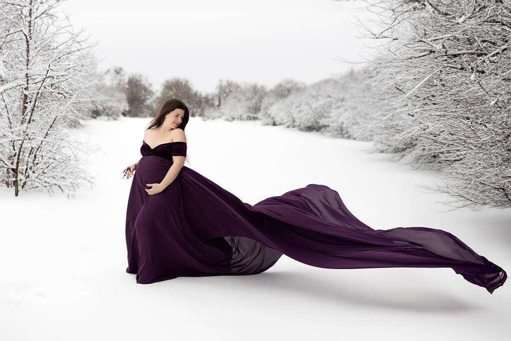 Une femme enceinte vêtue d'une robe violette dans la neige.