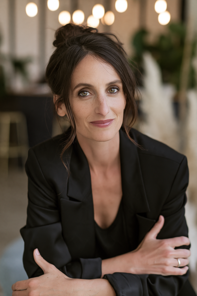 Portrait professionnel d’une femme en veston noir, bras croisés sur la table, regard confiant.