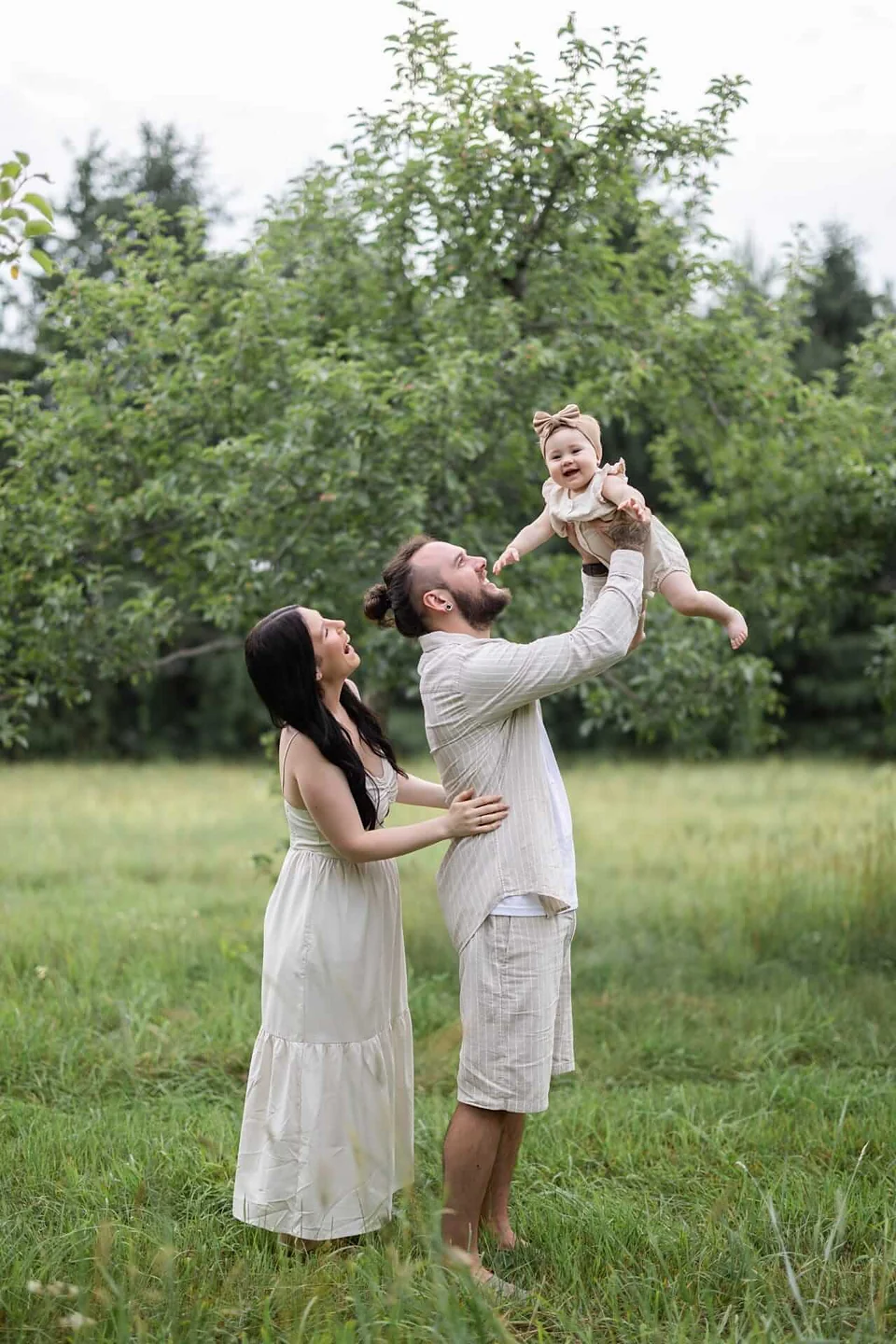 Photo d'une famille tenant leur bébé en l'air dans un verger de pommiers — Rébecca Vandal, photographe à Granby