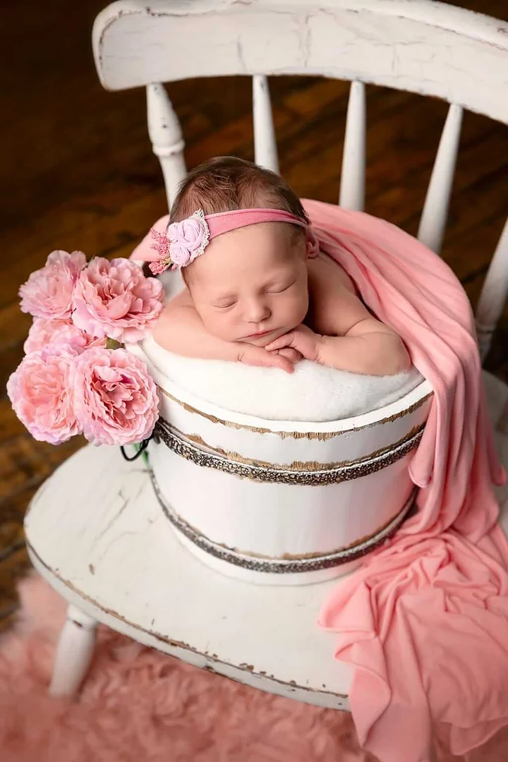Un bébé dormant dans un seau rose avec des fleurs roses