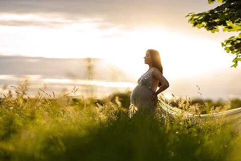 Une femme enceinte debout dans un champ au coucher du soleil.