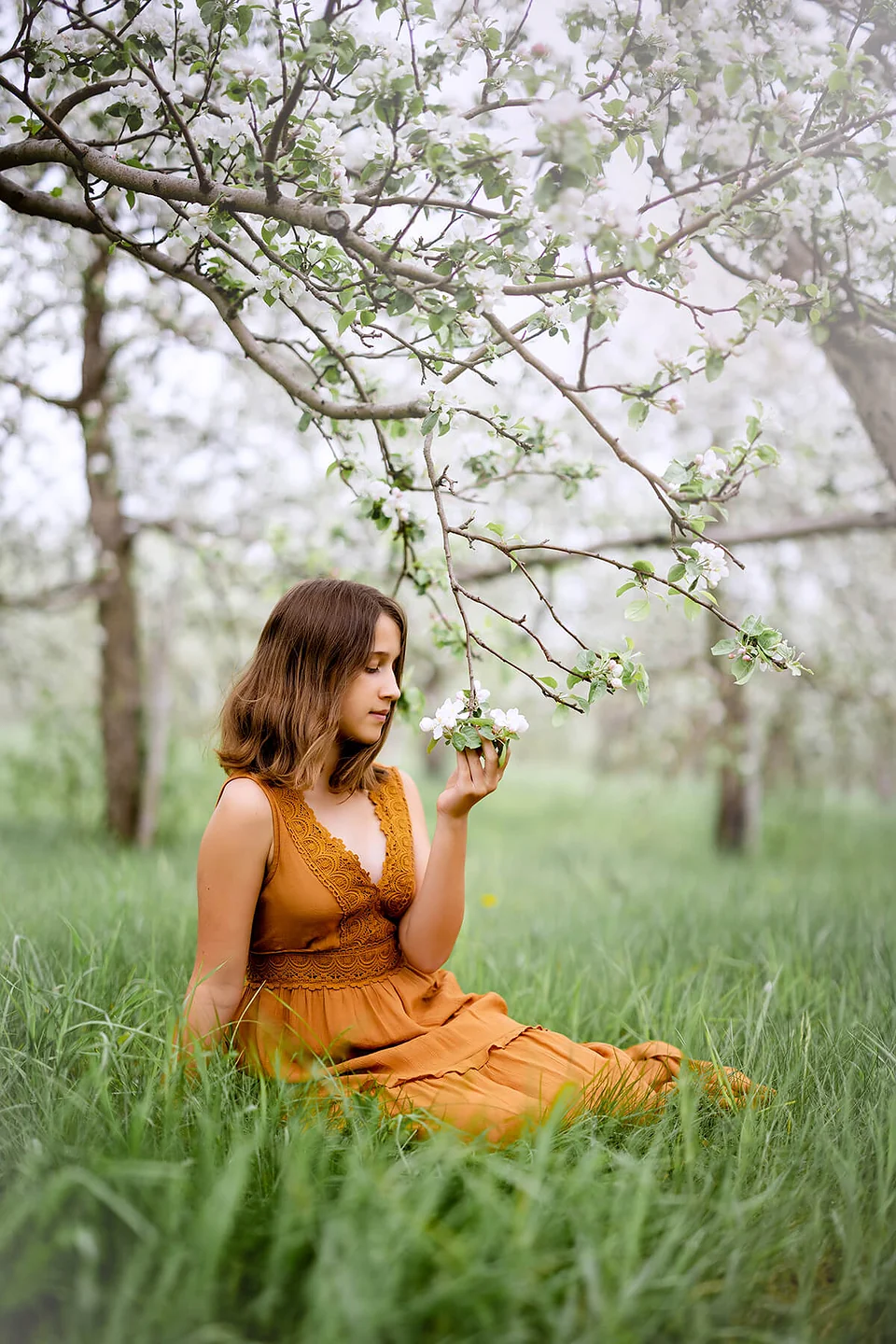 Une femme vêtue d’une robe orange assise dans un verger de pommiers — Rébecca Vandal, photographe à Granby